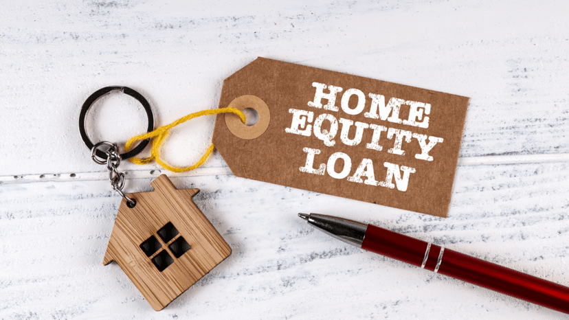 Brown tag labeled Home Equity Loan beside a wooden house keychain and red pen on a white surface