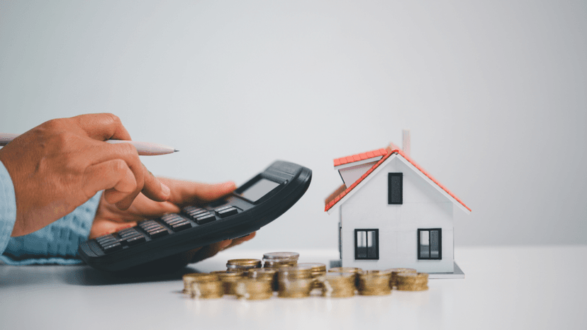 Person using a calculator next to a model home and stacked coins representing financial risk assessment for home equity borrowing